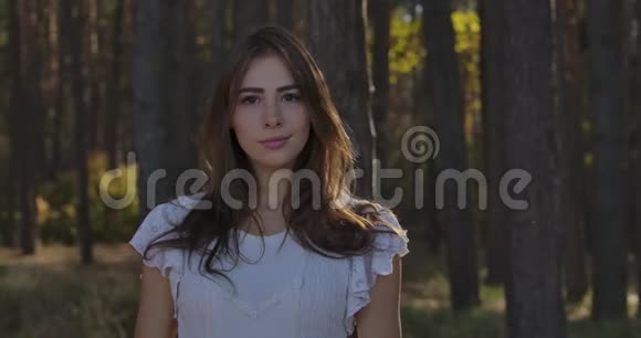 一个可爱的白种人黑发女孩的肖像棕色的眼睛站在夏季森林的树木之间妇女视频的预览图