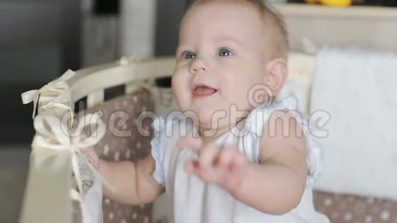 漂亮的婴儿站在婴儿床上可爱的女婴站在童床上大笑的肖像视频的预览图