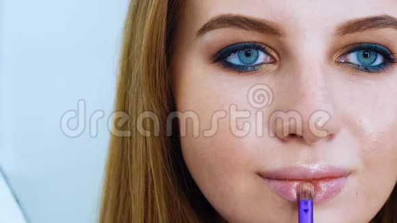 蓝眼睛红发化妆刷涂唇彩的年轻美女视频的预览图