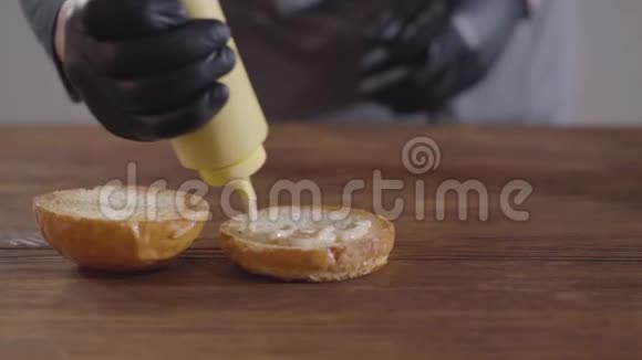 厨师的手在黑色厨房手套做汉堡特写厨师把黄色瓶子里的酱汁倒在视频的预览图