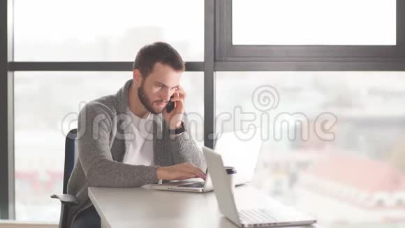 英俊的集中精力的企业家坐在同事的空间里使用笔记本电脑视频的预览图