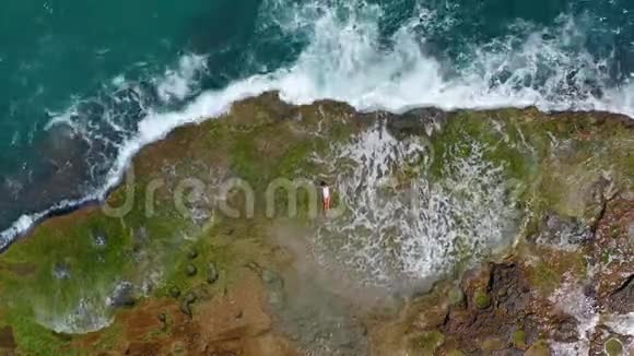 空气视图海浪溅起泡沫喷向石质海岸美丽的女人躺在岩石海滩上视频的预览图