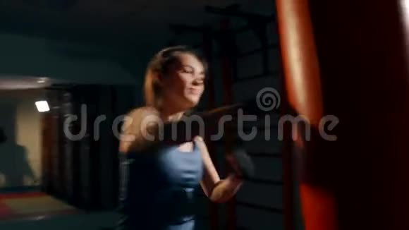 一个漂亮的女人对一个拳击袋进行猛烈的打击手持射击视频的预览图