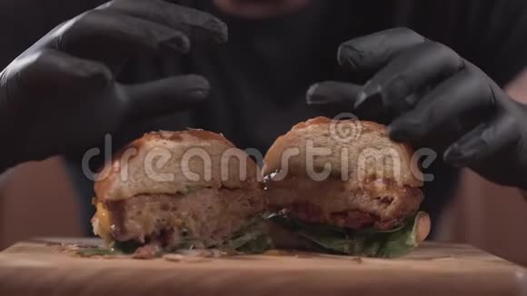 用黑色手套将半个美味的汉堡从木板上取出将男性的双手合上吃着口水的男人视频的预览图