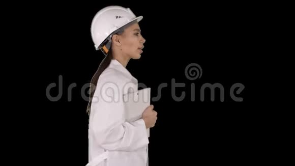 漂亮的西班牙裔妇女穿着白色的实验室外套和白色安全安全帽手提笔记本或平板电脑阿尔法频道视频的预览图