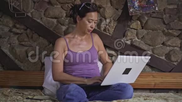 严肃的亚洲女人在家打手提电脑检查手机视频的预览图