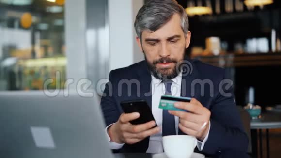在咖啡馆里用信用卡和智能手机进行网上支付的商人视频的预览图