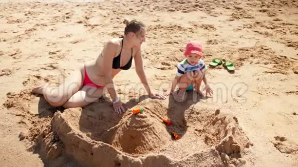 小母亲带着孩子坐在沙滩上的大沙堡的4k镜头视频的预览图