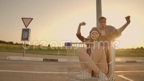 快乐的人日落时分一对夫妇一男一女骑在超市的手推车上慢行视频的预览图