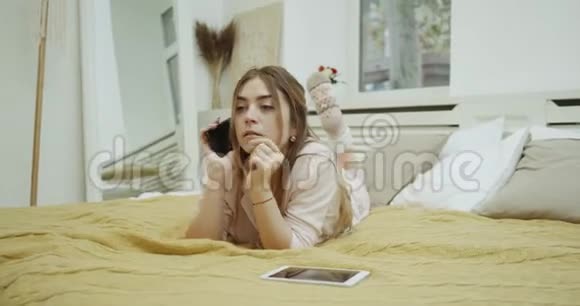 年轻女子打电话躺在舒适的床上穿着一件漂亮的睡衣视频的预览图