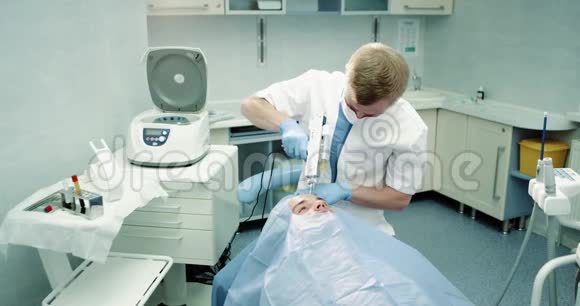 在一个现代化的诊所里医生做了一个带有微针的吸血鬼面部PRP手术病人坐在蓝色的上面视频的预览图