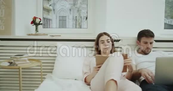 一对夫妇在一间现代化的卧室里在床上阅读和检查他们的笔记本4k视频的预览图