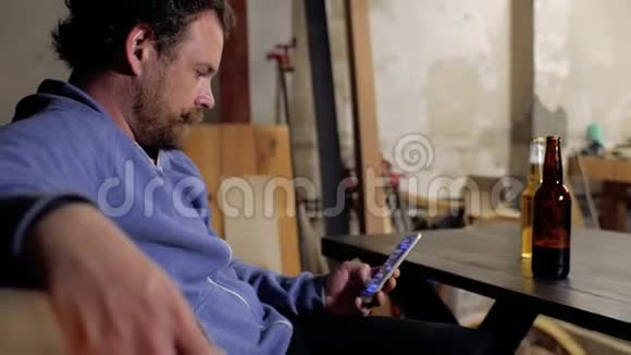 一个留着胡子和胡子的人正坐在桌旁用手机写短信面前的桌上放着两瓶视频的预览图