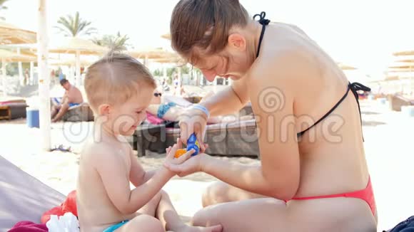 4k慢动作视频微笑的小男孩在沙滩上给年轻妈妈喷防晒霜视频的预览图