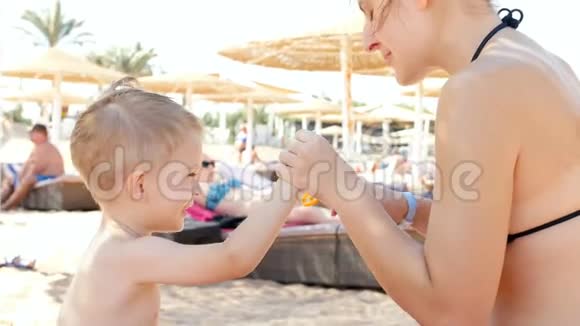 4k视频爱笑的孩子在沙滩上给年轻妈妈的鼻子涂防晒霜视频的预览图
