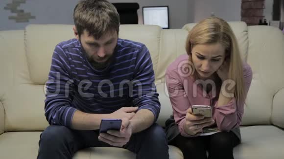 金发的妻子和丈夫坐在沙发上使用智能手机不互相注意视频的预览图