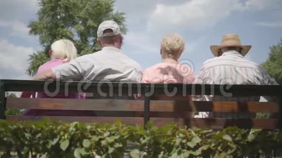 两对可爱的成熟夫妇坐在长凳上一起聊天成熟的人在户外休息资深人士视频的预览图