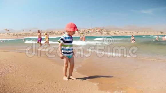 4k慢动作视频欢快的幼儿男孩站在海边玩海浪视频的预览图