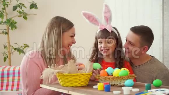一个年轻的家庭笑着高兴地向镜头展示复活节彩蛋桌子上有一个篮子里面有复活节彩蛋颜料和视频的预览图
