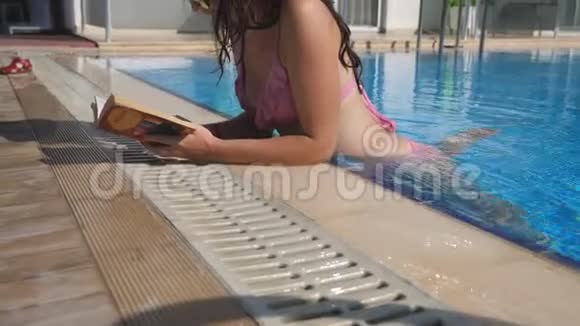 漂亮的女孩戴着帽子和太阳镜在游泳池看书年轻女子在假期里在温暖的阳光下放松视频的预览图