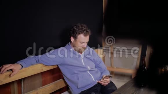 一个留着胡子和胡子的人正坐在桌旁用手机写短信面前的桌上放着两瓶视频的预览图
