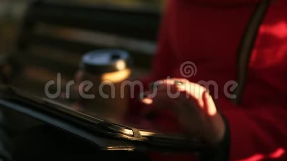 在秋天的天气里穿红色衣服的女人一只手拿着咖啡在公园里坐在长凳上打字红色视频的预览图