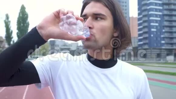 穿着运动衫的年轻人在体育场喝水头发黑的帅哥在一瓶酒后喝水视频的预览图
