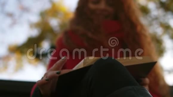 可爱的年轻女士的肖像长发卷曲的红色头发坐在长凳上在公园看书从低处拍摄视频的预览图