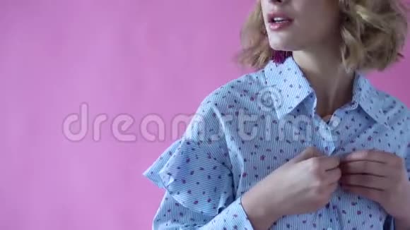 在一个粉色背景的摄影棚里一个开朗的金发女郎撩起她的衬衫视频的预览图