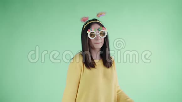 漂亮的年轻女子戴着滑稽的帽子和眼镜独自在绿色的背景上跳舞视频的预览图