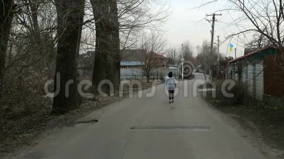 孤独的女人沿着马路走在房子和树之间视频的预览图