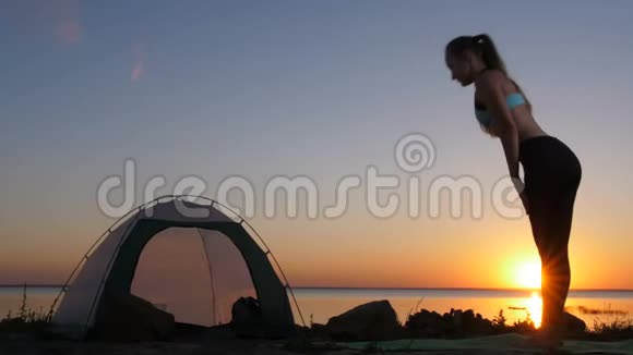 在日落时分露营时一个穿着向下狗姿势的女人视频的预览图