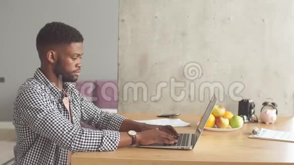 穿着休闲装的非洲男人坐在桌子前在家里打开笔记本电脑视频的预览图