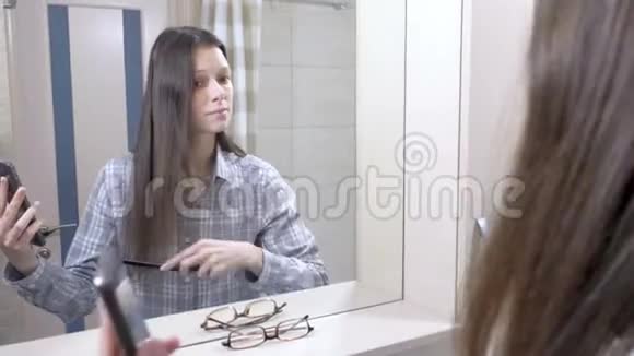 会说话的女人梳头站在浴室的镜子前看着手机视频的预览图