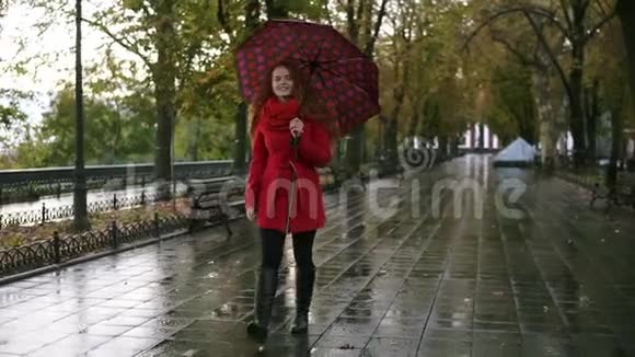 穿红衣服的女足在雨中撑伞行走红发女人穿着带伞的红色外套视频的预览图