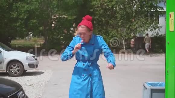 有趣的女孩在夏天吃冰淇淋金发女郎很有趣穿着一件蓝色的外套夏天戴着一顶红色的帽子幽默视频的预览图