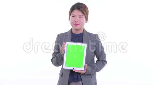 快乐的亚洲年轻女商人一边思考一边展示数码平板电脑视频的预览图