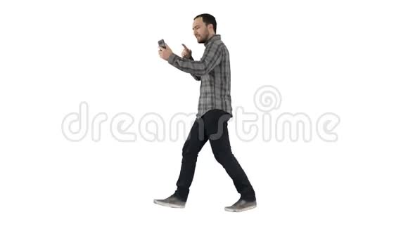 英俊的胡子男子用智能手机录制vlog博客同时在白色背景下行走视频的预览图