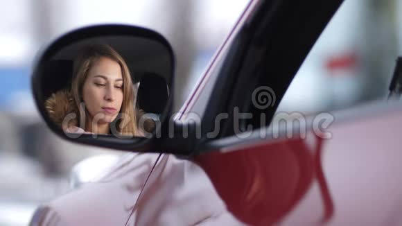 车里漂亮的女孩用粉红色的口红涂着她的嘴唇透过侧面的倒影看着相机视频的预览图