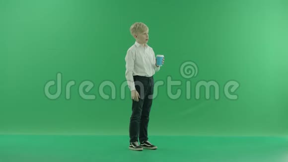 一个穿着校服的金发小男孩正拿着一杯咖啡或茶着他侧着身子站在视频的预览图