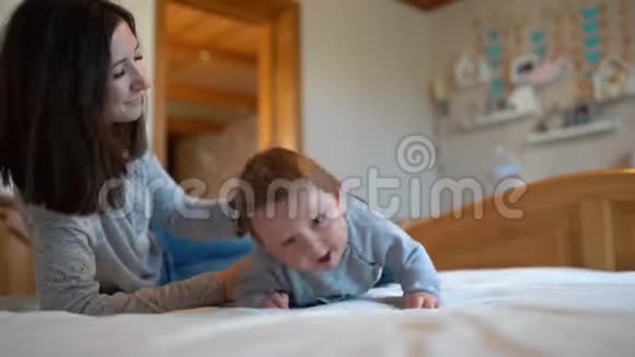 孩子和母亲在床上妈妈和小男孩在阳光明媚的卧室里玩父母和孩子在家放松家庭娱乐视频的预览图