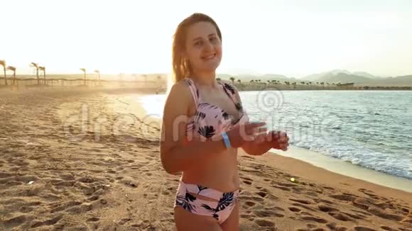 4k视频微笑年轻女子比基尼在海滩上的日落站在海边看镜头的少女视频的预览图
