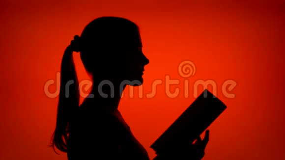 女性在红色背景下阅读物理印刷书的剪影女性的侧写研究视频的预览图