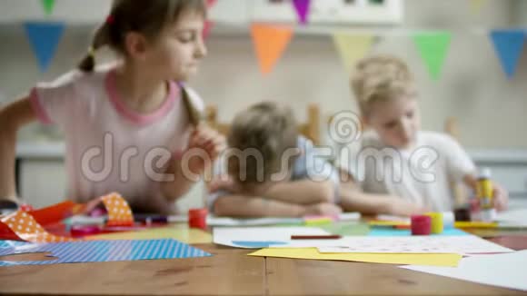 两个男孩和女孩坐在桌子旁一个躺在桌子上还用铅笔画画视频的预览图