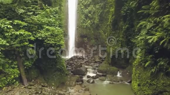 热带瀑布从热带雨林空中景观的岩石山中流淌出来在岩石瀑布上旅行的女孩视频的预览图