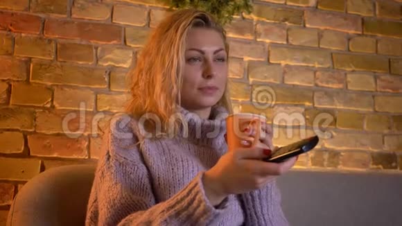 一位成年白种人金发女性在电视喜剧节目中坐着喝热茶的特写镜头视频的预览图