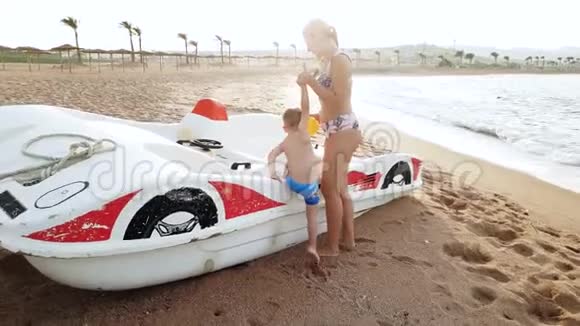 4k段小母亲帮助小儿子爬在双体船上站在海边视频的预览图