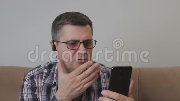 一个中年男人坐在沙发上用智能手机里的视频通话与另一个人交流视频的预览图