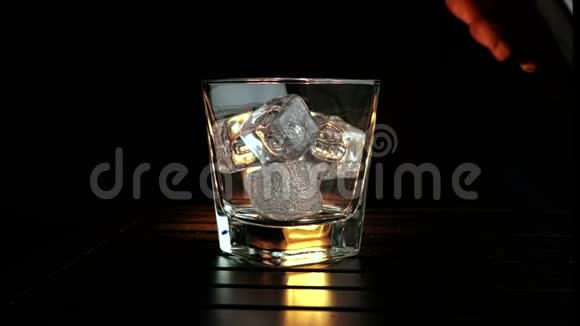 酒吧老板把威士忌倒在杯子里木桌上放冰块黑黑的背景重点放在冰块上威士忌放松时间视频的预览图