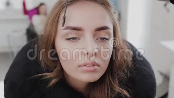 专业化妆师用一个漂亮女孩的特殊眉毛刷梳眉毛美女客户视频的预览图